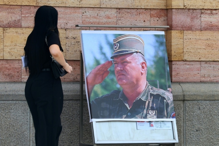<p>Une femme regarde un portrait de l'ancien chef militaire des Serbes de Bosnie, Ratko Mladić, devant la cathédrale orthodoxe de Banja Luka, en Bosnie, le 28 août 2026, au lendemain de sa mort à l'âge de 84 ans dans un hôpital pénitentiaire de La Haye</p>